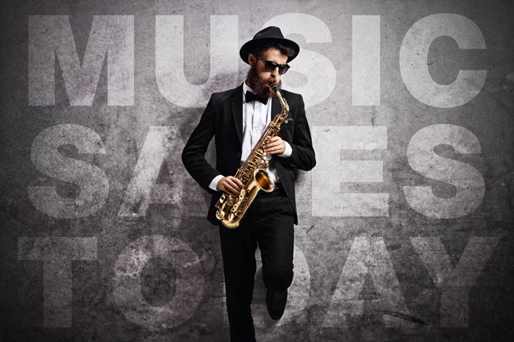 saxophonist in tux, hat and sunglasses playing in front of a wall that says music saves today